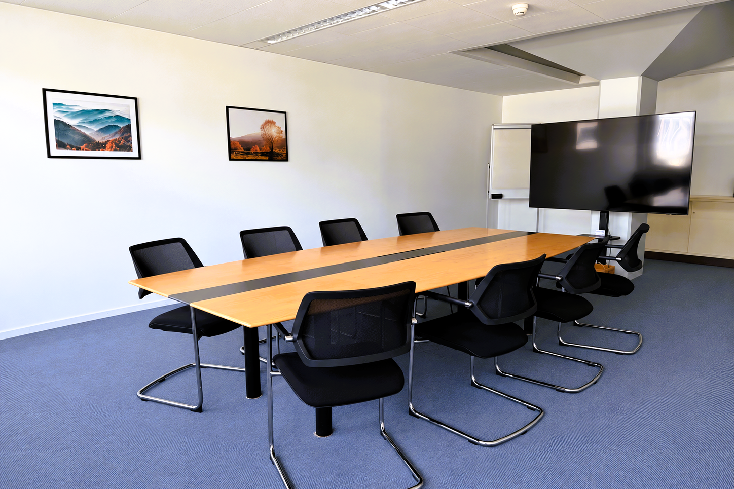 Heller Sitzungsraum mit Konferenztisch, schwarzer Bestuhlung und grossem Präsentationsbildschirm
